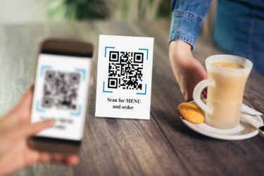 Women's hands are using the phone to scan the qr code to select menu. Scan to get discounts or pay for coffee. The concept of using a phone to transfer money or paying money online without cash.FAKE QR.QR codes/barcodes in the image not contain offensive language, brand names, or links to websites or products.